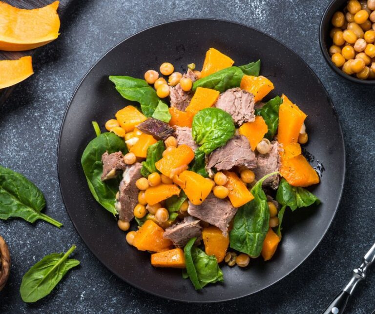 A warm chickpea, pumpkin, spinach, and beef salad on a dark countertop.