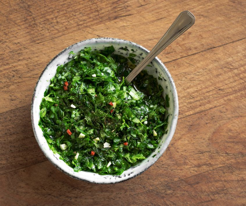 Bright green Chimichurri Sauce in a white bowl on a wooden table.