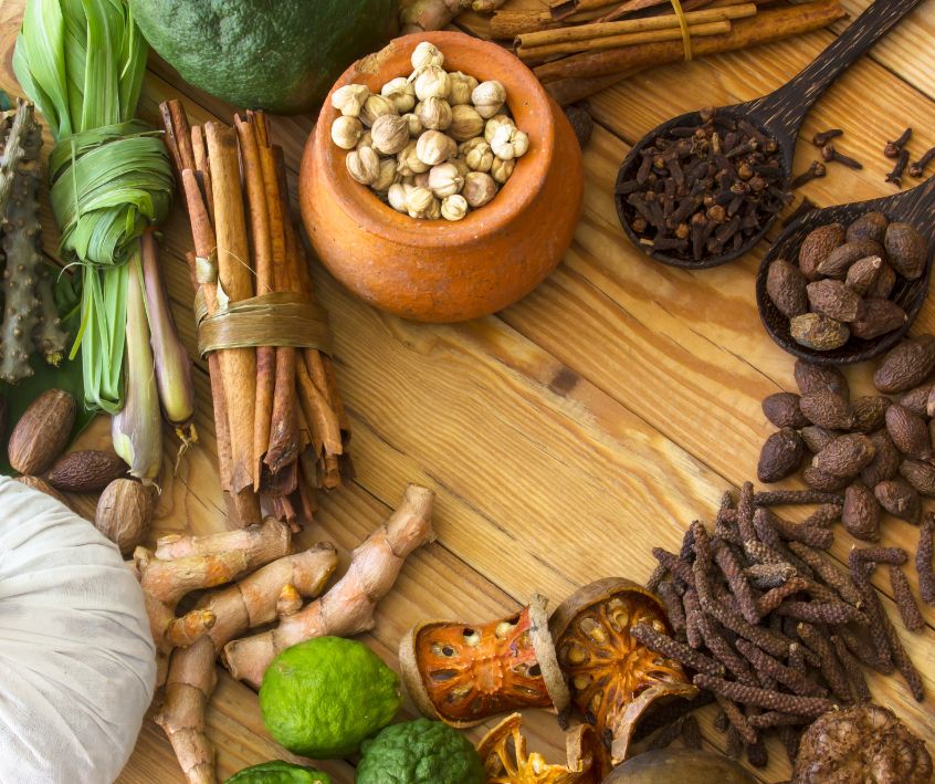 A wooden table with a mix of dried and fresh aromatic spices on it.