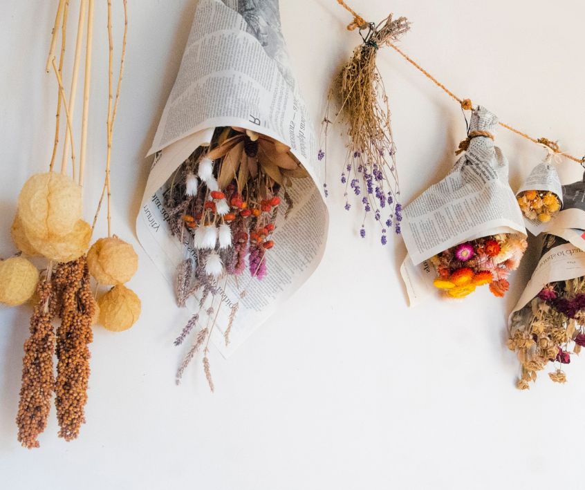 Drying garden flowers and seed heads wrapped in newspaper paper hanging from brown twine.