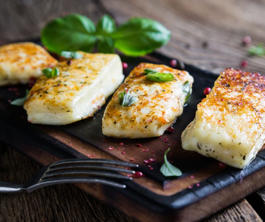 Grilled halloumi cheese portions on a dark severing plater with fresh green basil.