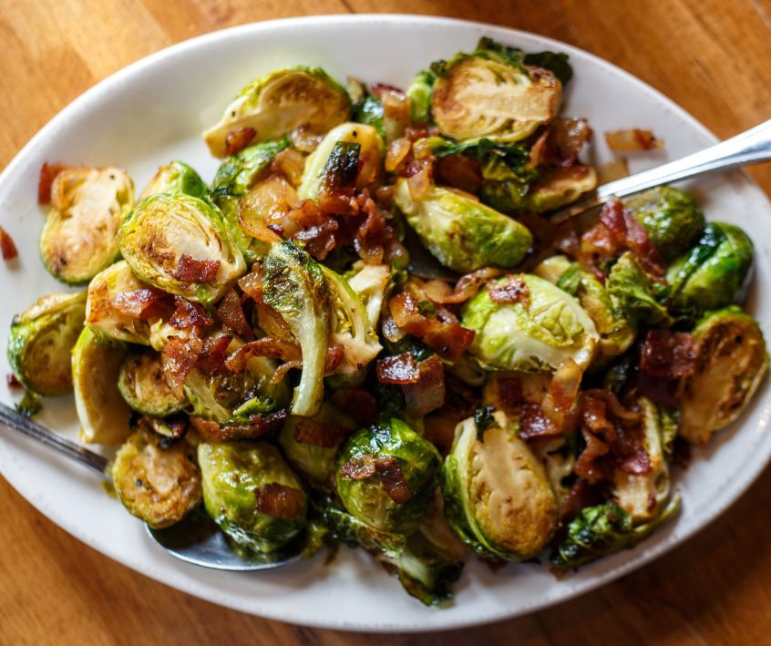 Roasted Brussels Sprouts with Bacon on a white plate with two spoons.