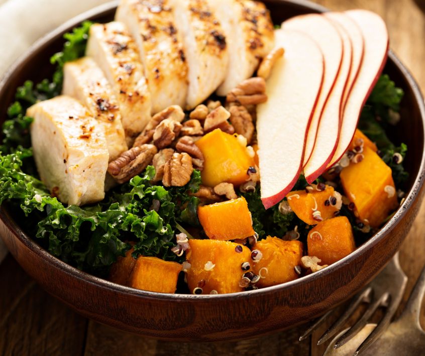 Warm quinoa kale sweet potato chicken salad in a dark earthenware bowl.