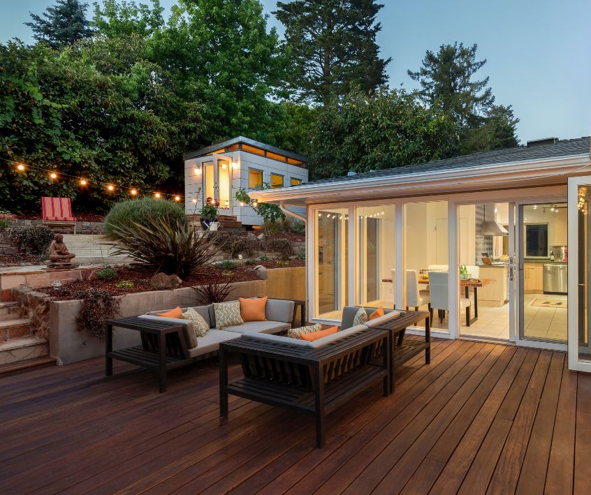A large wooden deck with multiple sitting areas next to a large green privacy fence.