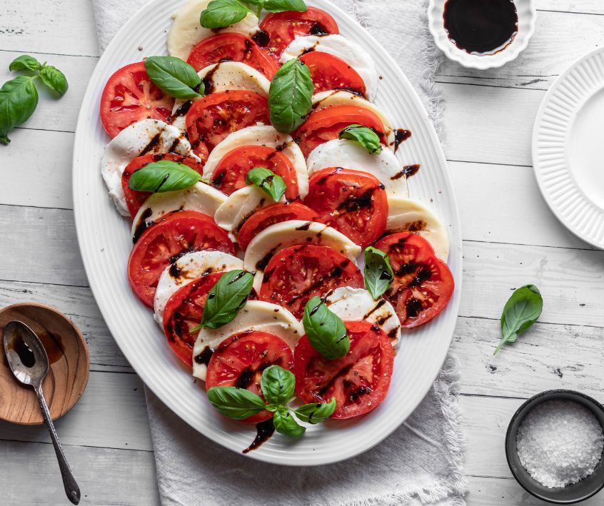 A beautifully arranged Caprese salad topped with basil and balsamic glaze.