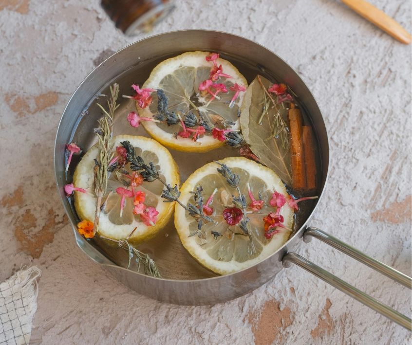 Lemon slices, cinnamon sticks, and mixed herbs and flowers in a metal pot.