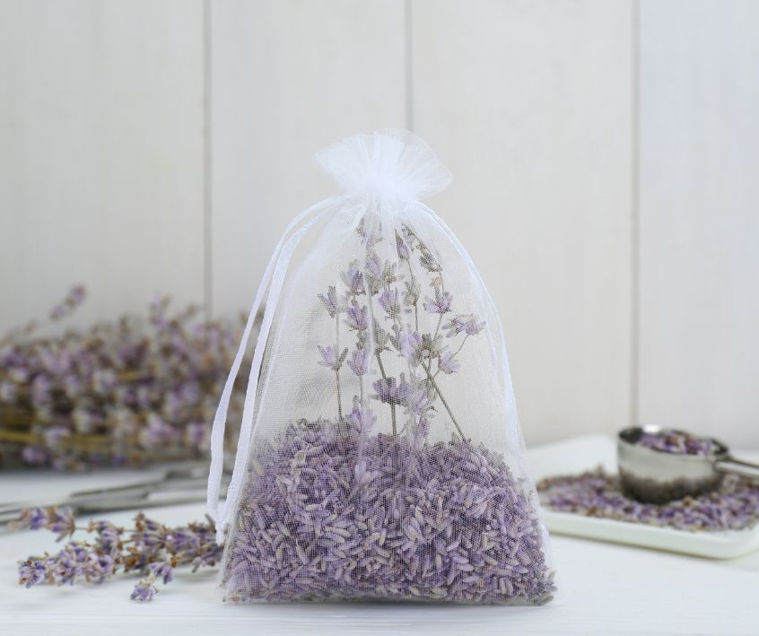 Dried lavender flowers in a white organza bag on a table with dried flower sprigs.