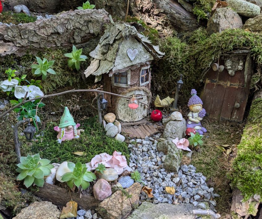 Small fairy garden and mini town with faiefolk at the base of a tree.