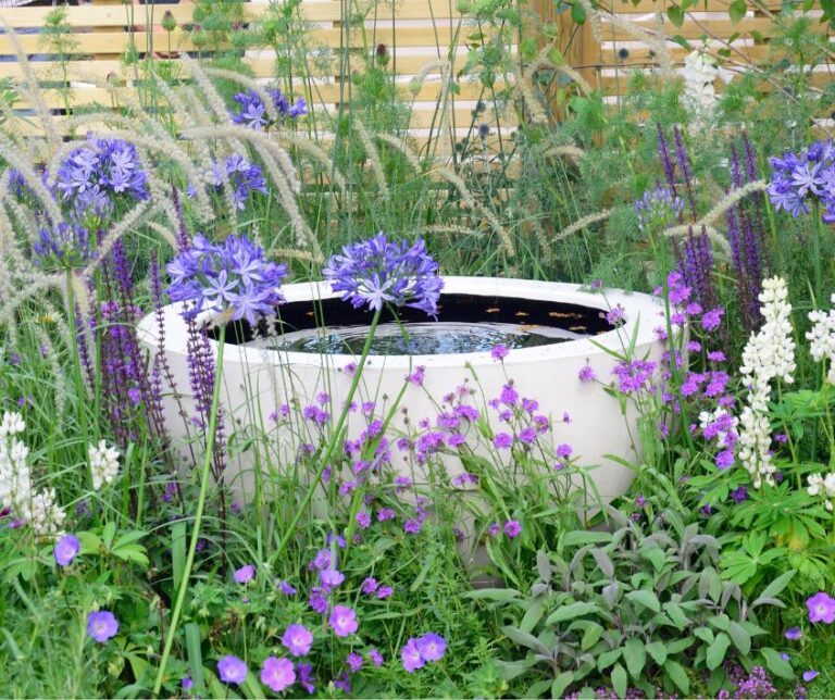 Garden water feature surrounded by purple flowers.