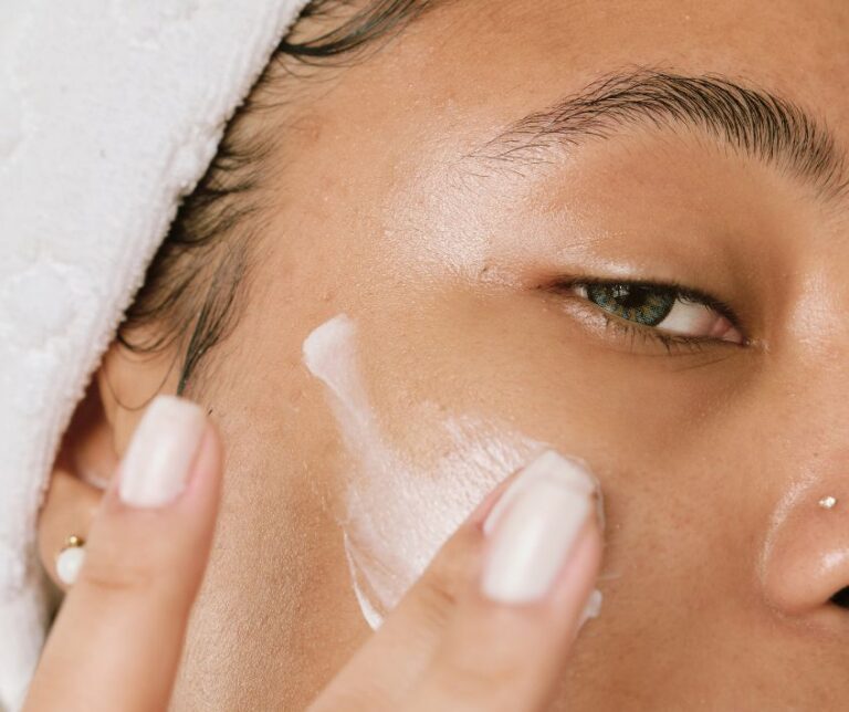 A woman applying a white cream to her face with her fingers.