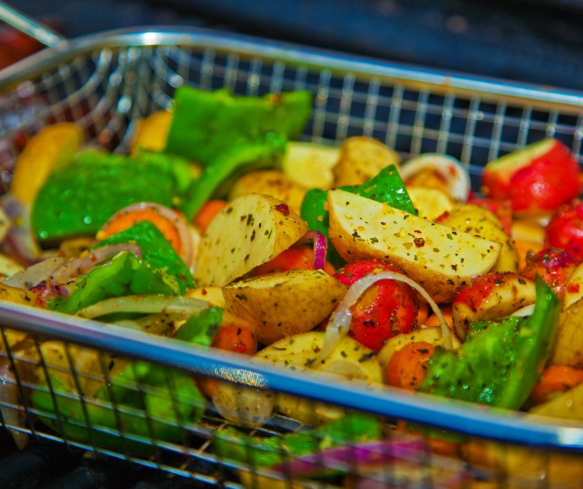 A bright mix of veggies cooking in a grill basket.