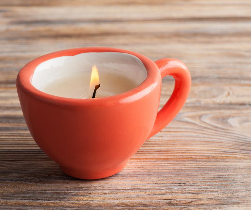 An orange ceramic teacup that has been turned into a candle on a table top.