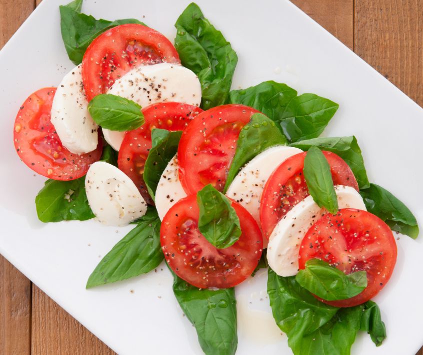 Slices of fresh tomato, white mozzarella, and basil on a white plate.