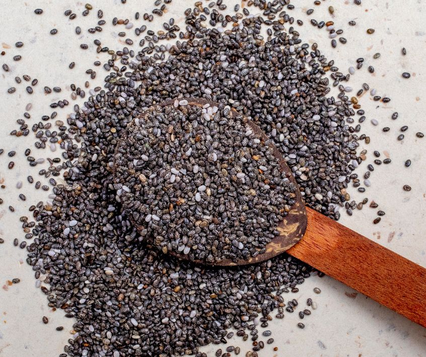 A wooden spoon on a white counter covered in tiny black chia seeds.