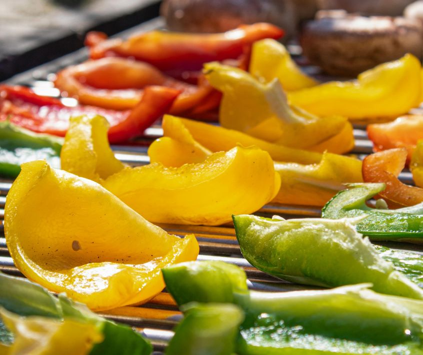 Sliced red, yellow and green bell peppers next to mushrooms on a grill.