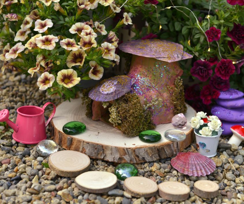 Tiny garden tools, and pathway in a small fairy garden surrounded by flowers.
