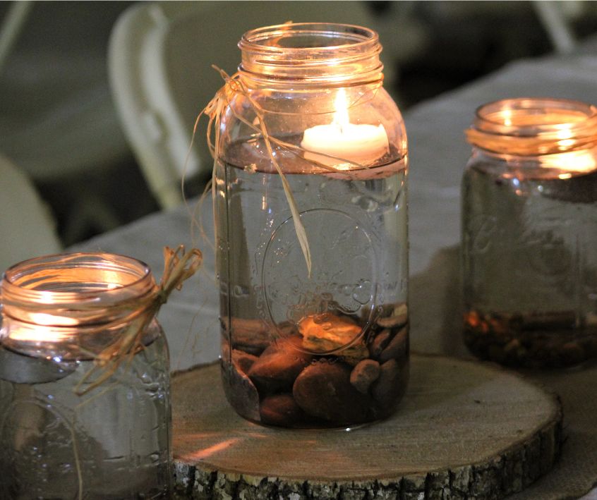 A trio of mason jar lanterns featuring floating candles, a burlap ties and river pebbles.