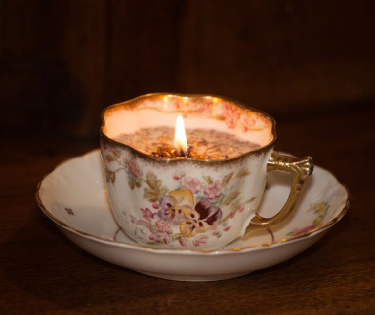 A vintage tea cup and saucer candle burning on a wooden table.