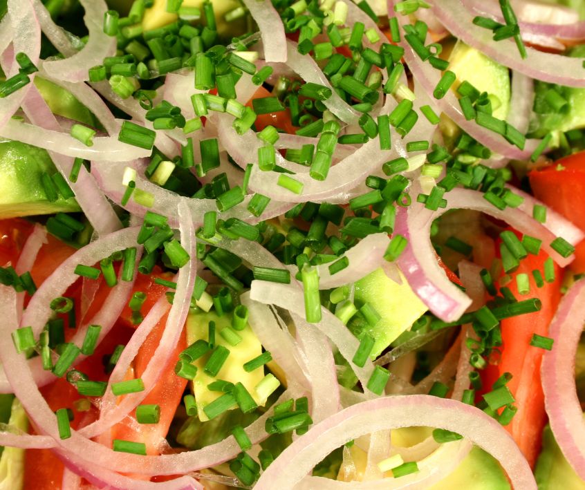 Diced chives on a red onion, avocado and tomato salad.