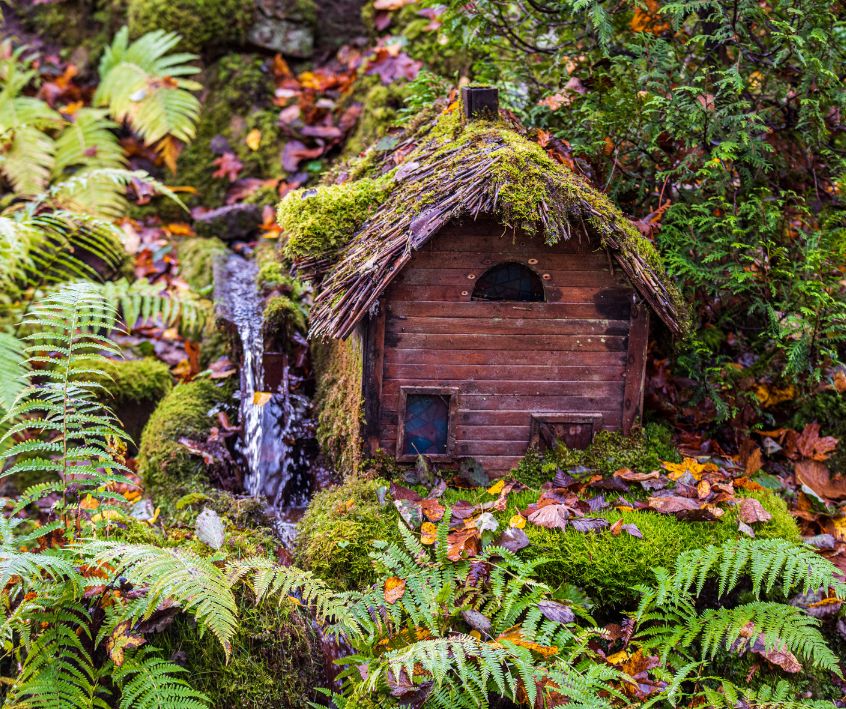 A wooden fairy cottage surrounded by green foliage.