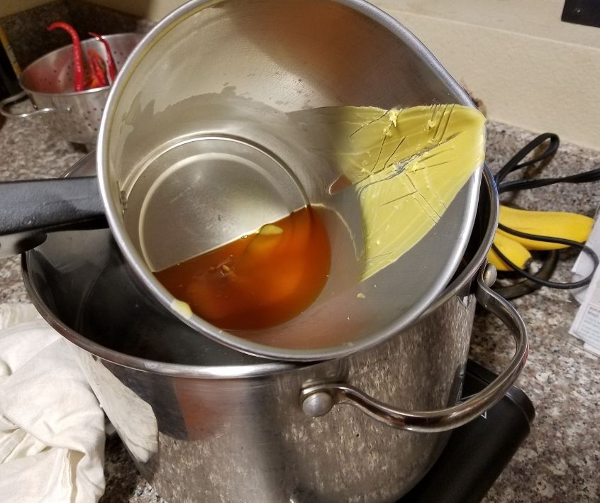 A wax pouring pitcher melting beeswax over a pot of hot water on a hot plate.