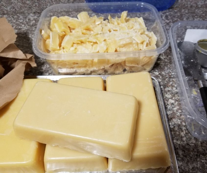 Light beeswax in rectangular bars next to a container of beeswax chunks on a kitchen counter.