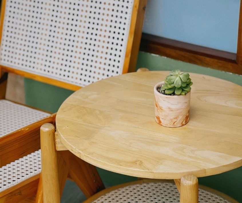 A simple wooden chair with a wicker back next to a circular wooden table with a small potted succulent plant on it.