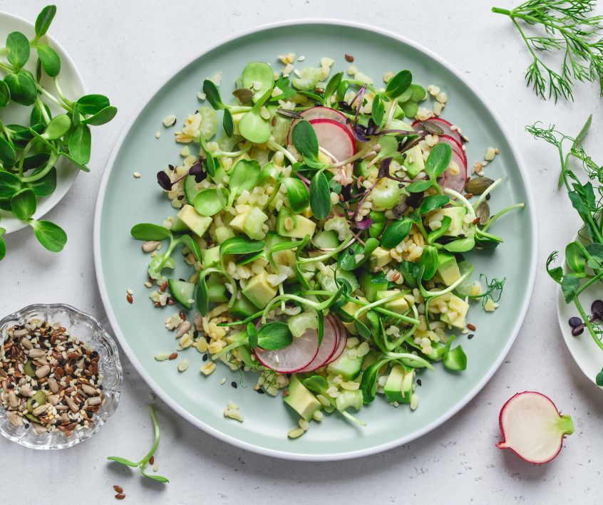 A light blue plate with a simple mixed salad topped with pea and sunflower microgreens on it.