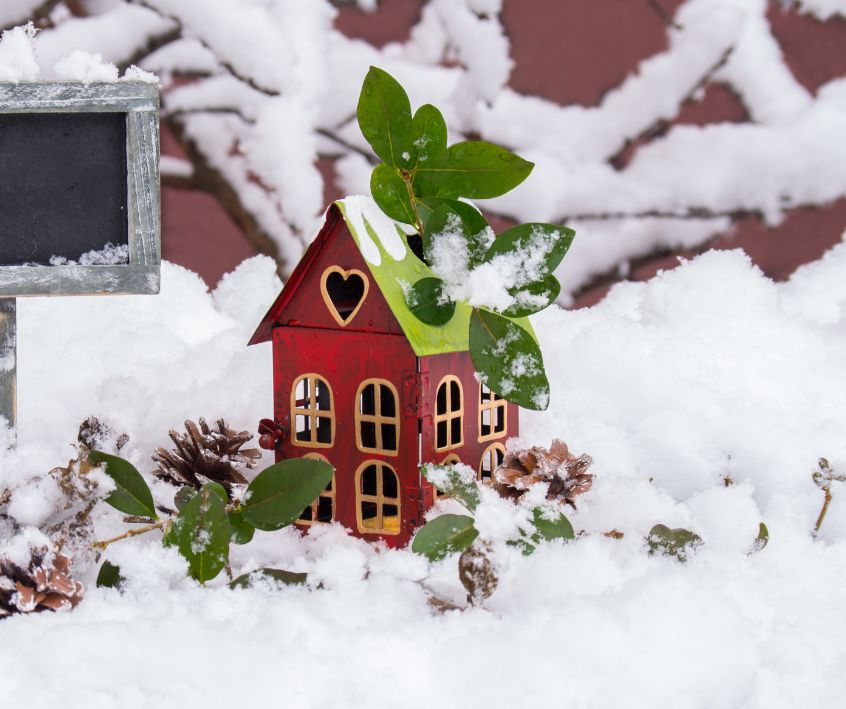 A small red and green fairy house in snow next to a board for inspirational messages.