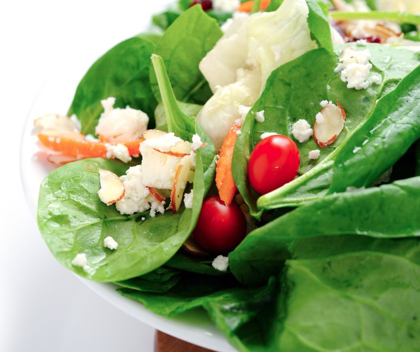 Spinach leaves in a salad bowl topped with feta crumbles, cherry tomatoes, and almond slivers.