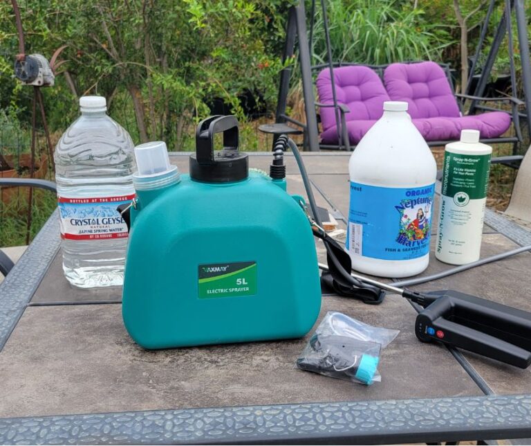 Liquid garden fertilizer, a bottle of water, and the green Vaxmay battery powered garden sprayer on a patio table.