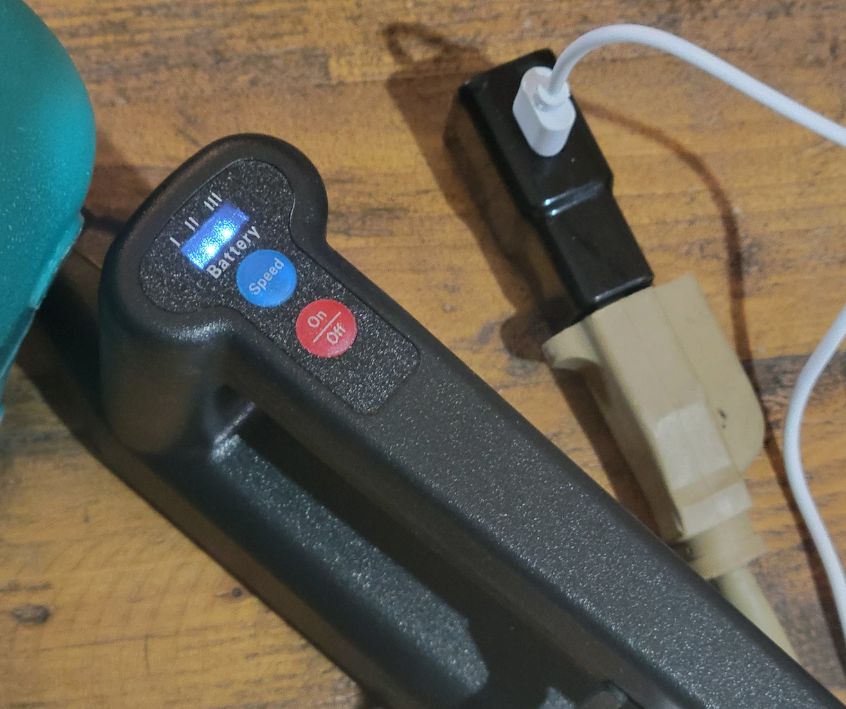 A black sprayer wand plugged into a charger on a wooden table.