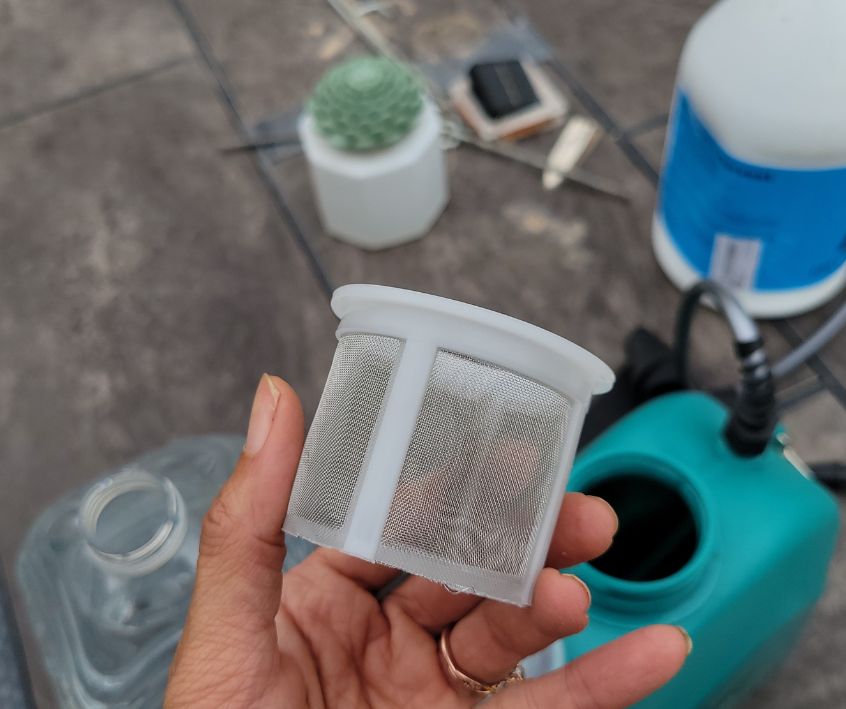 A hand holding the filter cup above the Vaxmay Electric Sprayer.