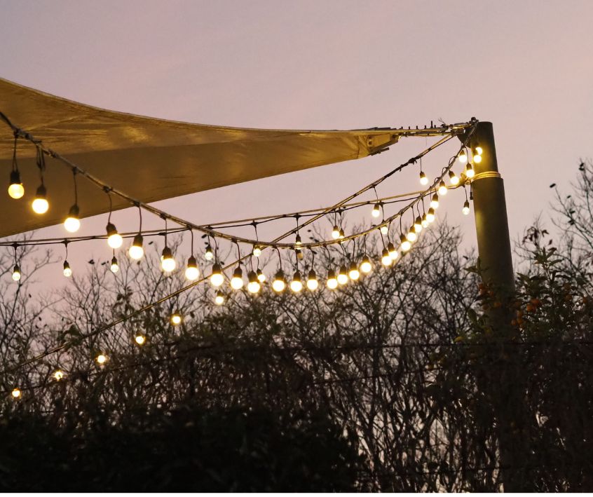 A backyard shade sail with string lights on it at dusk.